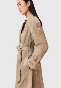 Μπεζ τζιν μπουφάν από σουέντ με ζώνη στη μέση, μεγάλα πέτα και μανσέτες με κουμπιά. Διαθέτει πλαϊνές τσέπες και κομψή, εφαρμο στή γραμμή.