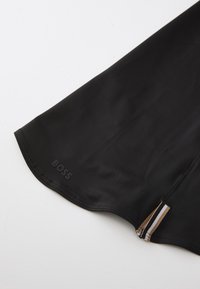 Fekete szövet ruha sima textúrával, lekerekített hemzéssel, és logóval az alsó szélén. Cipzáras díszítések csíkokkal az oldalon.