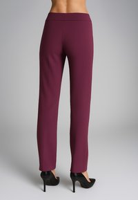 Pantaloni tailored bordeaux con una consistenza liscia, caratterizzati da un design a gamba dritta e un alto punto vita, abbinati a tacchi alti neri.