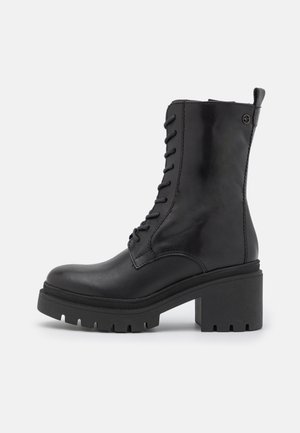 Svart läderankelstövlett med snörning fram, klumpig platåsula och liten klack. Slät textur med förstärkta sömmar och flik.