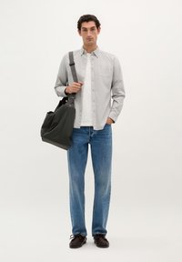 O cămașă gri cu maneci lungi purtată peste un tricou alb, asortată cu blugi albaștri și pantofi închiși la culoare. O geantă de umăr neagră completează ținuta.