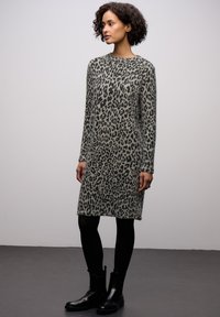 Abito lavorato a maglia di colore grigio chiaro con stampa leopardata scura, con maniche lunghe, scollatura a girocollo e una vestibilità comoda, abbinato a stivali neri alla caviglia.