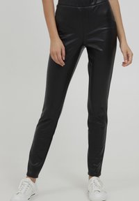 Zwarte faux leren leggings met een slim fit, een gladde textuur, hoge tailleband en een minimalistisch ontwerp, gecombineerd met witte sneakers.