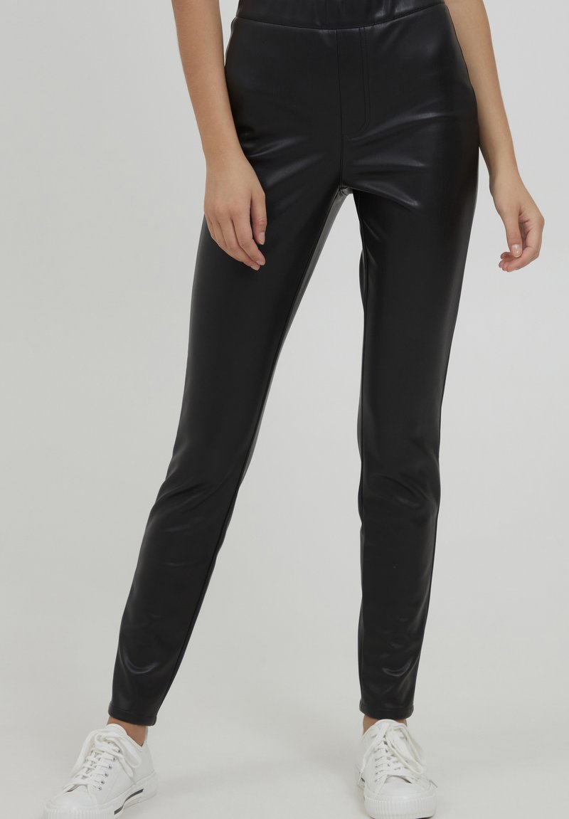 Zwarte faux leren leggings met een slim fit, een gladde textuur, hoge tailleband en een minimalistisch ontwerp, gecombineerd met witte sneakers.