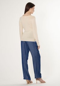 Helle beige Langarmbluse mit einem runden Rückenausschnitt, kombiniert mit lockeren blauen Denim-Hosen und hautfarbenen Absatzsandalen. Weicher Stoff und lässiges Design.
