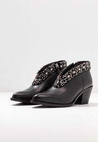 Botas de tobillo de cuero negro con una decoración de cuentas y embellishments de rhinestone en la parte superior y un tacón mediano apilado.