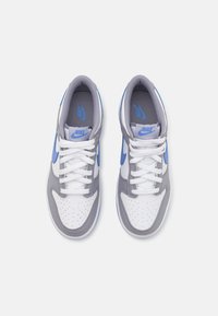 Nike-sko med hvitt skinn på overdelen, grå semsket skinn-detaljer og blå Nike-swoosh, flate hvite lisser og perforert tå-design.