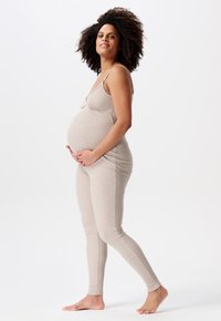 Beige ribbet graviditetstanktop og leggings, tætsiddende design, blød tekstur, båret af en kvinde, der holder om sin gravide mave, barfodet.