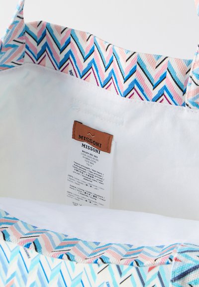 Εσωτερικό τσάντας tote με πολύχρωμο σχέδιο ζιγκ-ζαγκ, λευκή επένδυση και υφασμάτινη ετικέτα που γράφει "MISSONI" με οδηγίες φροντίδας.