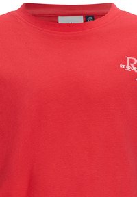 Rotes Baumwoll-T-Shirt mit kurzen Ärmeln und Rundhalsausschnitt. Mit einem weißen Logo-Druck im linken Brustbereich. Glatte Textur.