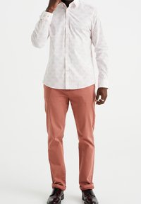 Camisa blanca de botones con un patrón geométrico rosa, combinada con pantalones rosa claro y zapatos negros brillantes. Ajuste casual, mangas largas.