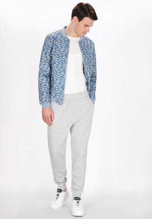 Blauwe bomberjack met vispatroon, wit T-shirt, grijze joggers en witte sneakers. Lichte stof en relaxte pasvorm met ribgebreide manchetten.