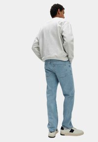 Sudadera gris, jeans de corte relajado en azul claro y zapatillas blancas con detalles negros; visto desde atrás.