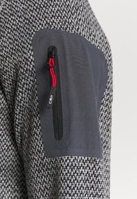 Szary materiał w wzory z jednolitym ciemnoszarym łatą na ramieniu. Posiada kieszeń na zamek z czerwonymi akcentami i firmową zawieszką.