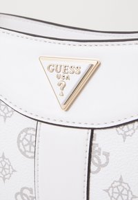 Borsa sintetica bianca con un logo triangolare dorato con la scritta "GUESS USA", accentuata da modelli geometrici grigi e rifiniture nere a contrasto.
