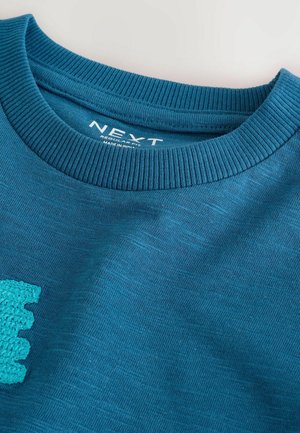 Türkisfarbener Baumwoll-Sweatshirt mit geripptem Rundhalsausschnitt und einem strukturierten türkisfarbenen Häkelmuster auf der Vorderseite. Das Etikett zeigt "NEXT".