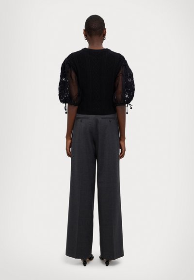 Černý pletený svetr s vzorovanými balónovými rukávy, doplněný o šedé široké kalhoty s vysokým pasem. Měkká textura, minimální detaily.