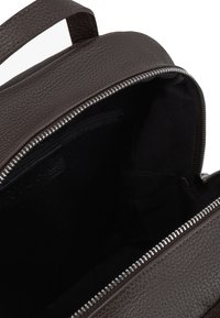 Rucsac din piele texturată de culoare maro închis, deschis pentru a arăta interiorul dintr-o țesătură neagră și dinții metalici argintii ai fermoarului de-a lungul deschiderii.