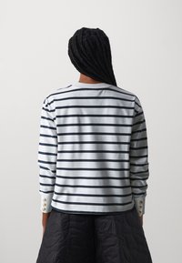 Camiseta de manga larga a rayas en azul claro con rayas azul marino, con detalles de botones en los puños. Material suave de algodón, ajuste relajado.