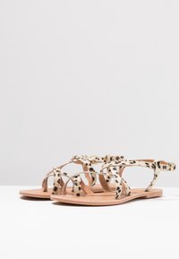 Sandály s leopardím vzorem, ploché s překříženými pásky, béžovým základem a hladkým povrchem. Mají zapínání na sponu a minimalistický design.