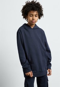Navyblauwe capuchontrui gemaakt van een zachte katoenmix, met een voorzak en ribgebreide manchetten, en subtiele logodetails op de borst.