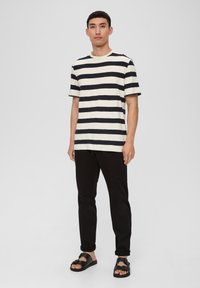 Camiseta de manga corta a rayas en color crema y marino, con cuello redondo, combinada con pantalones negros y sandalias negras con hebilla.