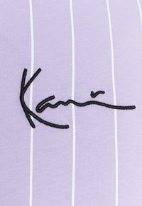 Purple fabric featuring vertical white stripes, with a prominent embroidered black signature, adding texture and contrast to the design.