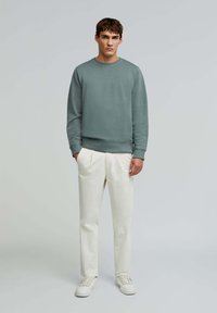 Jasnozielony sweter z okrągłym dekoltem i prążkowanymi mankietami, zestawiony z kremowymi spodniami i białymi sneakersami. Prosty, casualowy design.