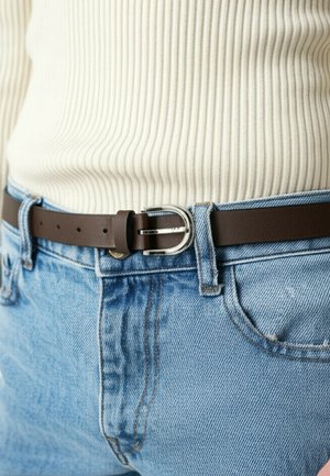 Brown leather belt with a silver rectangular buckle, worn over light blue denim jeans. Ribbed white top visible above the belt.