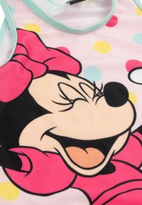 Top da bagno senza maniche rosa con il volto sorridente di un grande personaggio, rifinito con una bordatura verde menta e pois multicolori su uno sfondo chiaro.