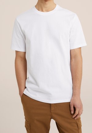 Biała bawełniana koszulka z okrągłym dekoltem i krótkimi rękawami, w połączeniu z brązowymi spodniami, prezentująca luźny krój i gładką fakturę.