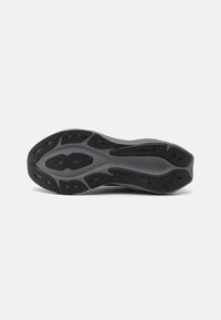 Semelle de chaussure de sport noire en caoutchouc texturé, présentant des rainures profondes et un accent central lisse et légèrement surélevé pour une meilleure traction.