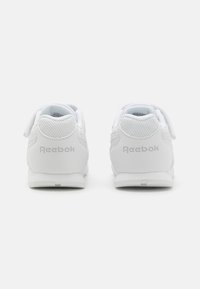 Hvite atletiske sko med mesh-detaljer og gummisåler. Bakfra vises "Reebok"-merkevaren i sølv. Borrelåsene er fremtredende for feste.