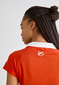 Rode sportieve polo met een witte kraag en korte mouwen. Heeft een klein wit Nike-logo met een laurierontwerp op de achterkant.