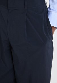 Navy blue pants with a smooth fabric, featuring a flat front, side pockets, and a subtle sheen. Tapered design with tailored fit.