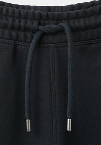 Schwarzer elastischer Bund mit gebundenem schwarzem Kordelzug mit Metallenden, auf schwarze Stoffhose genäht.