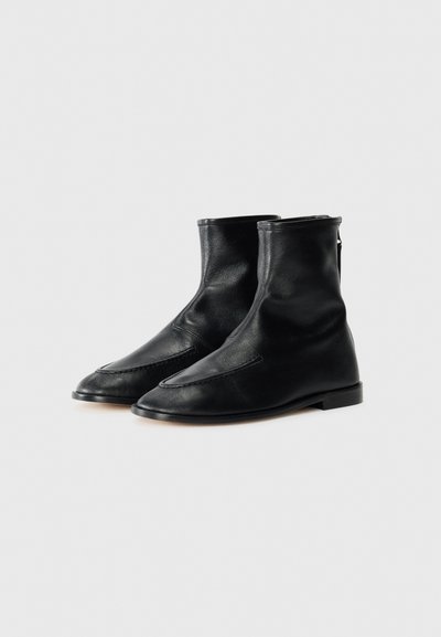 Bottines en cuir noir avec un design élégant, bout pointu, couture minimale et un talon bas et plat. Présente une fermeture éclair à l'arrière.