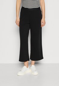 Czarne szerokie spodnie z miękkiego materiału, z wysokim stanem. W zestawie z białymi trampkami. Częściowo widoczny pasiasty top.