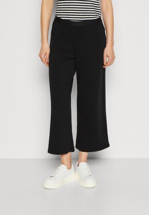 Svarta vida byxor i mjukt material, med hög midja. I kombination med vita sneakers. Randig överdel delvis synlig.