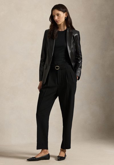 Melns ādas žakete pār pieguļošu melnu topu, kombinēts ar augstām vidukļa melnajām biksēm un plakanām melnām kurpēm. Minimāla aparatūra un pielāgots dizains.