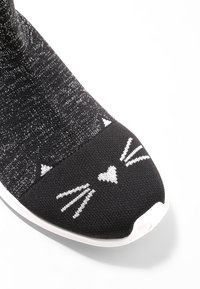 Schwarze Strick-Sneaker mit einem Katzenkopfdesign auf der Zehe, ausgestattet mit weißen Schnurrhaaren und einem Herz, ergänzt durch eine weiße Gummisohle.