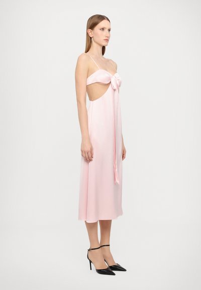 Vestido de satén rosa pálido con un corsé ajustado, cortes en los laterales y un detalle de lazo en el delantero, combinado con tacones de aguja negros.