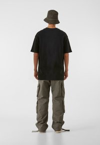 Črna oversize majica s sproščenim krojem, v kombinaciji s khaki cargo hlačami, ki imajo stranske žepke. Dopolnjena z pleteno vedro klobukom.