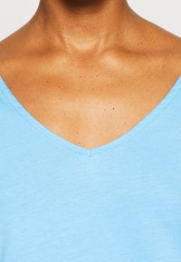 Světle modrý bavlněný top s výstřihem do V, který se vyznačuje hladkou texturou, krátkými rukávy a čistým švem kolem výstřihu.