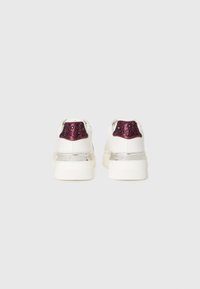 Et par hvide sneakers med tykke såler, metalforkromede hæl accenter og lilla paillet hæl lapper mod en neutral baggrund.