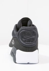 Svart sneaker med strukturerat tygöverdrag, vadderad häl och vit gummisula. Utrustad med en upphöjd Nike AIR-logotyp och en distinkt bakdesign.