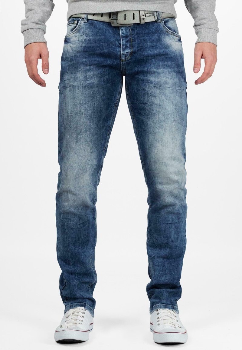 Blauwe denim jeans met een vervaagde afwerking, rechte pijpen, vijf zakken en een grijze riem. Witte sneakers maken de look compleet.