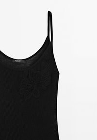 Schwarzes ärmelloses Oberteil mit geribbelter Textur. Verfügt über ein florales Stickdetails auf der linken Seite und dünne Träger. Etikett im Inneren sichtbar.