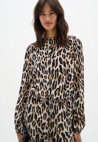 Bluza s leopardjim vzorcem iz lahkega materiala, dolge rokave, visok ovratnik in elastične manšete, z detajlom kravate na pasu.