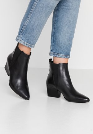 Botas de cuero negras hasta el tobillo con puntera afilada, paneles laterales elásticos y tacón cuadrado. Combinadas con unos vaqueros azul claro con dobladillo.